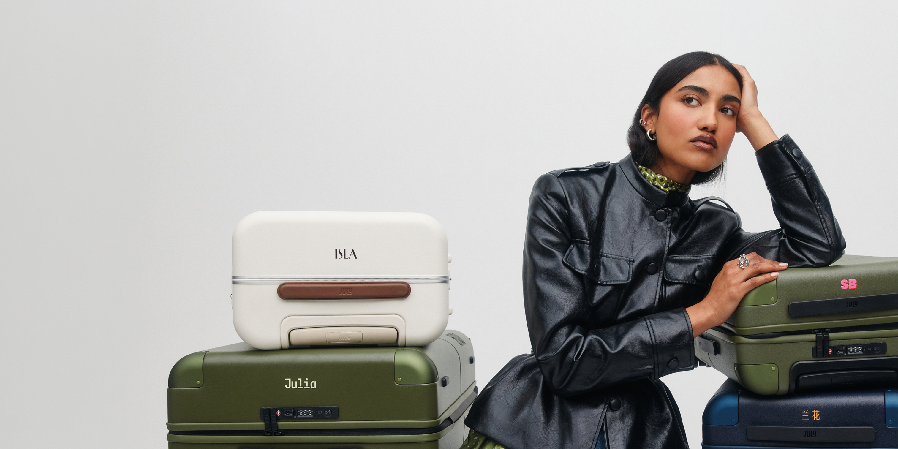 Woman in a black leather jacket leaning on July suitcases personalised with the monograms ISLA and Julia