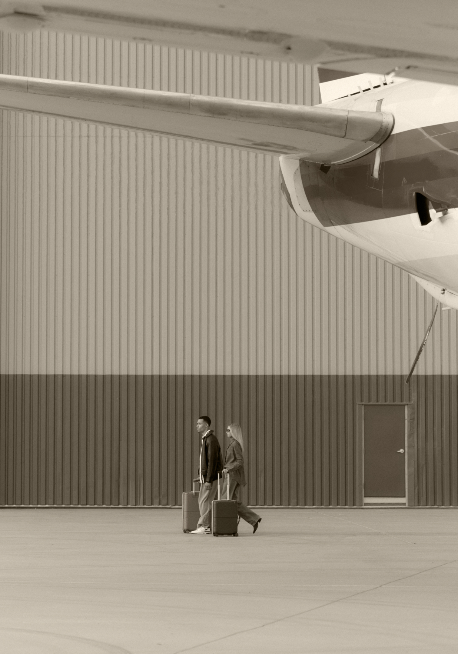 Two travellers crossing a hangar with their luggage
