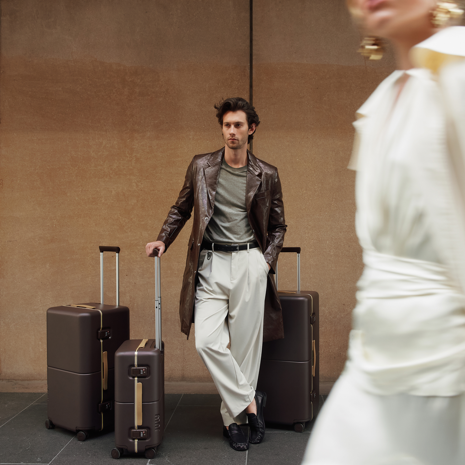 Man in a leather coat leaning on July Trunk suitcases