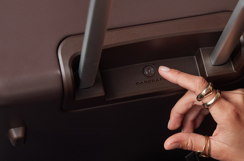 Finger pressing the CaseSafe button on a July Trunk suitcase