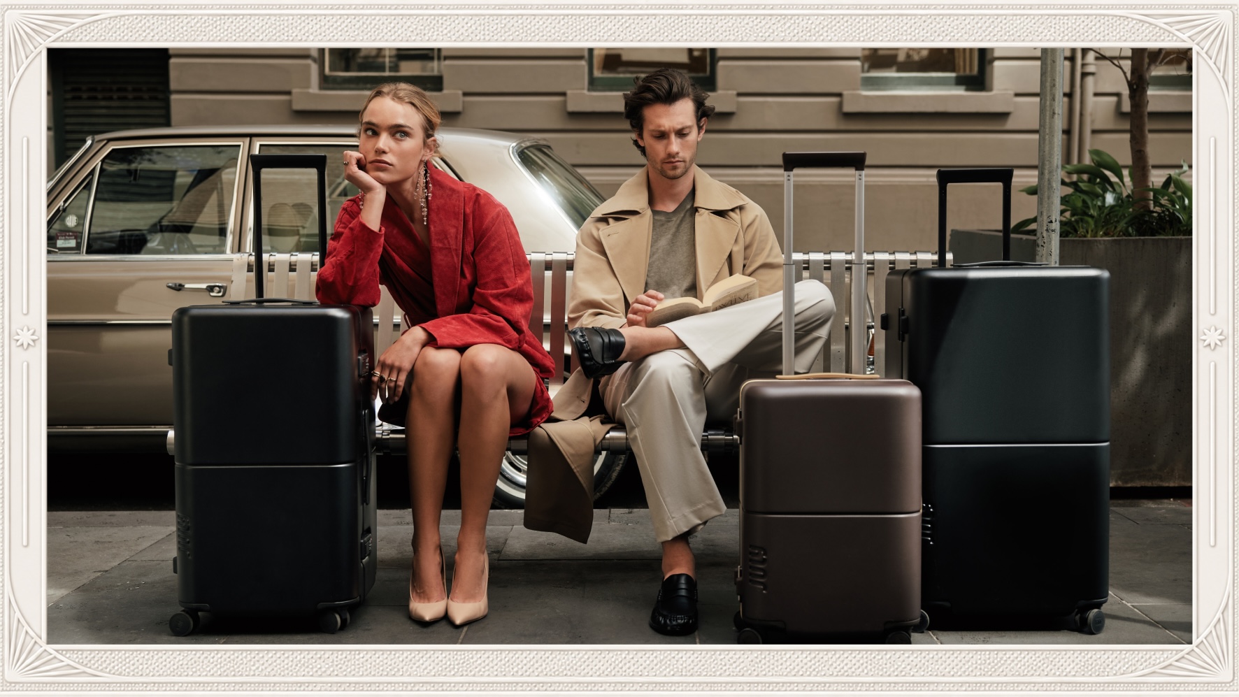 Two travellers seated on a city bench beside July Trunk suitcases