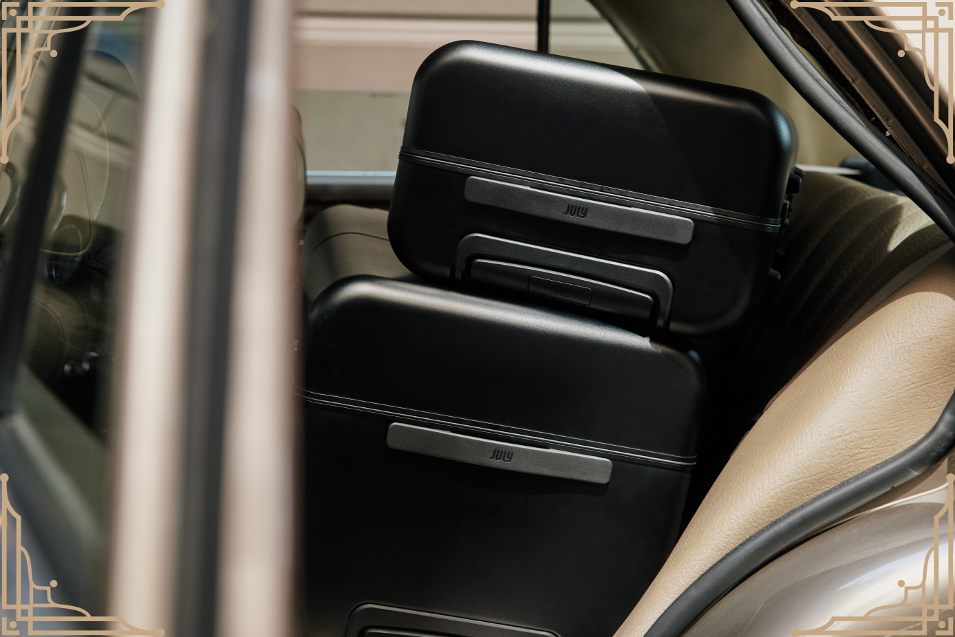 Two black July Trunks stacked on the back seat of a vintage car