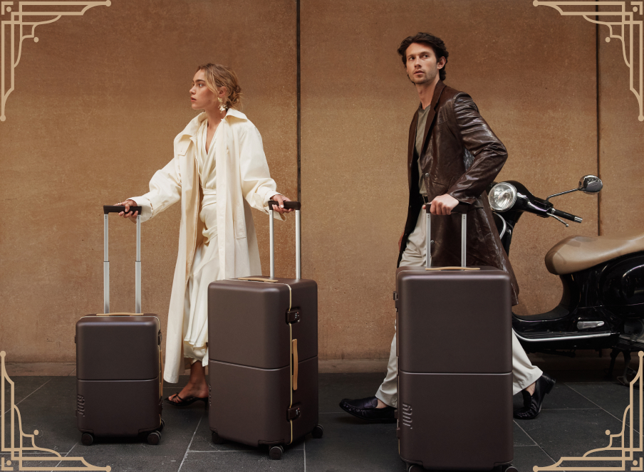 Two travellers wheeling brown July Trunks past a parked scooter